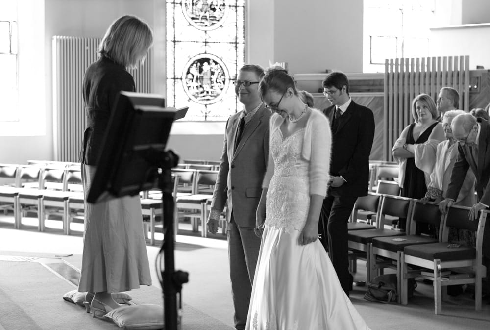 Bride and groom smiling at minister’s words during ceremony, black and white photo.