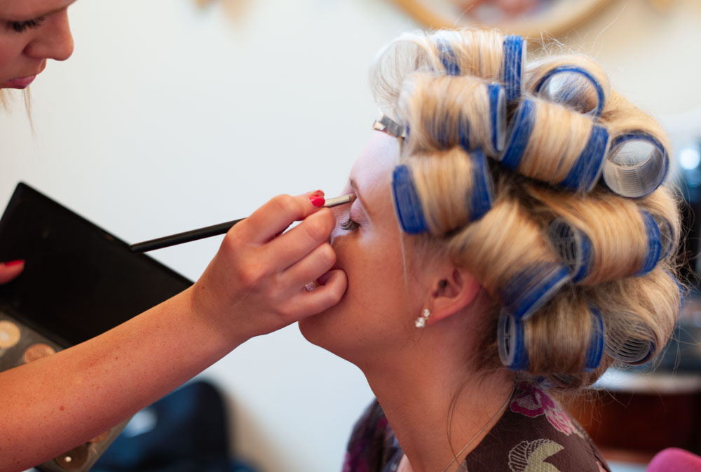 Side profile of the bride in curlers as her eye makeup is carefully applied.