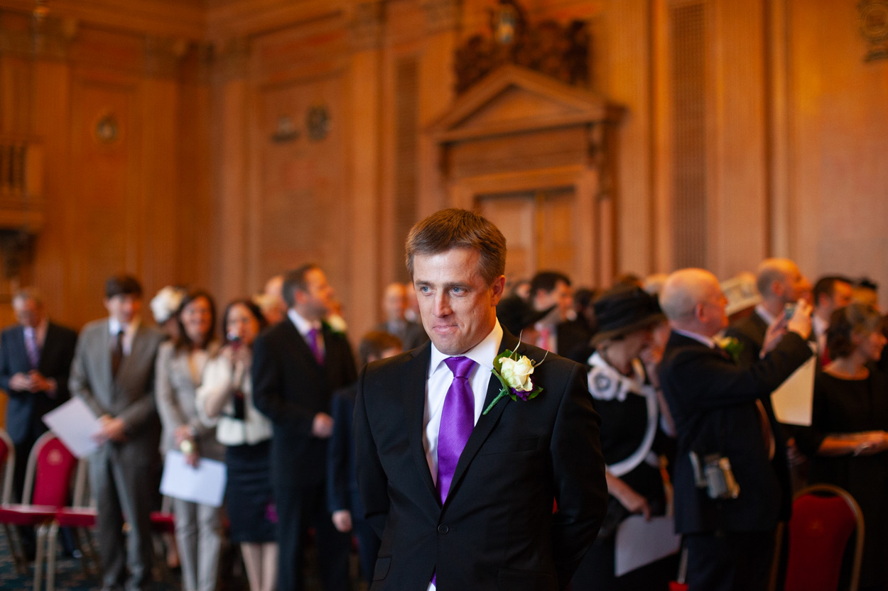 Groom standing as guests rise in anticipation of the bride’s arrival.