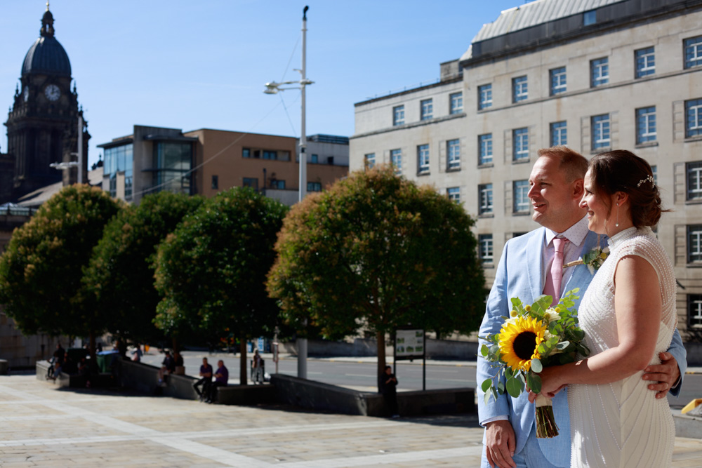 Couple posed naturally on the steps of Leeds Civic Hall - Gemma & Danny look across Leeds Civic Hall - a row of 4 green trees and Leeds Civic Hall in the background. A Perfect Tuesday wedding in Leeds City Centre