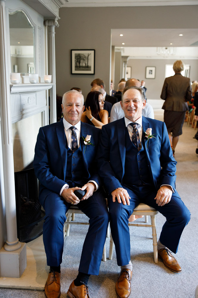 Groom seated beside his best man in blue suits and brown shoes