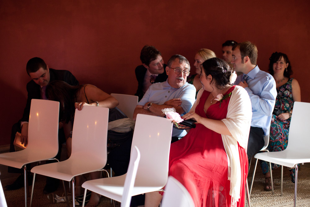 Guests seated on white chairs chatting inside the red-walled ceremony space