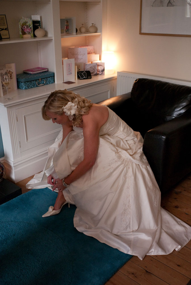 Dani fastens the buckles on her wedding shoes in a black chair