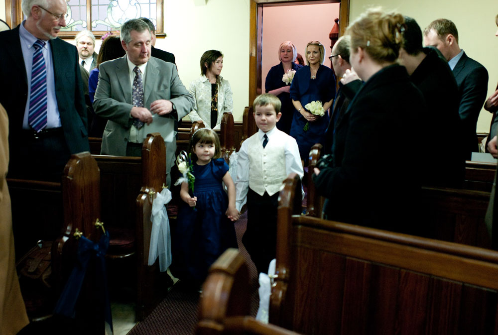 Flower girl, page boy, and bridesmaids walk down the aisle of the church.