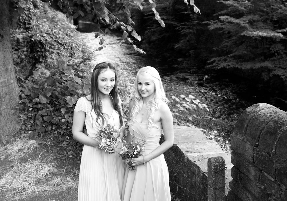 Two bridesmaids captured from above in black and white, stream flowing behind them.