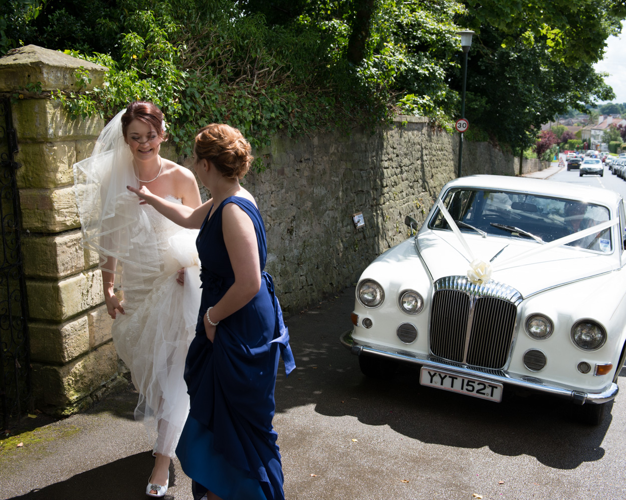 Bride arrives in a vintage white Rolls as a bridesmaid adjusts her veil