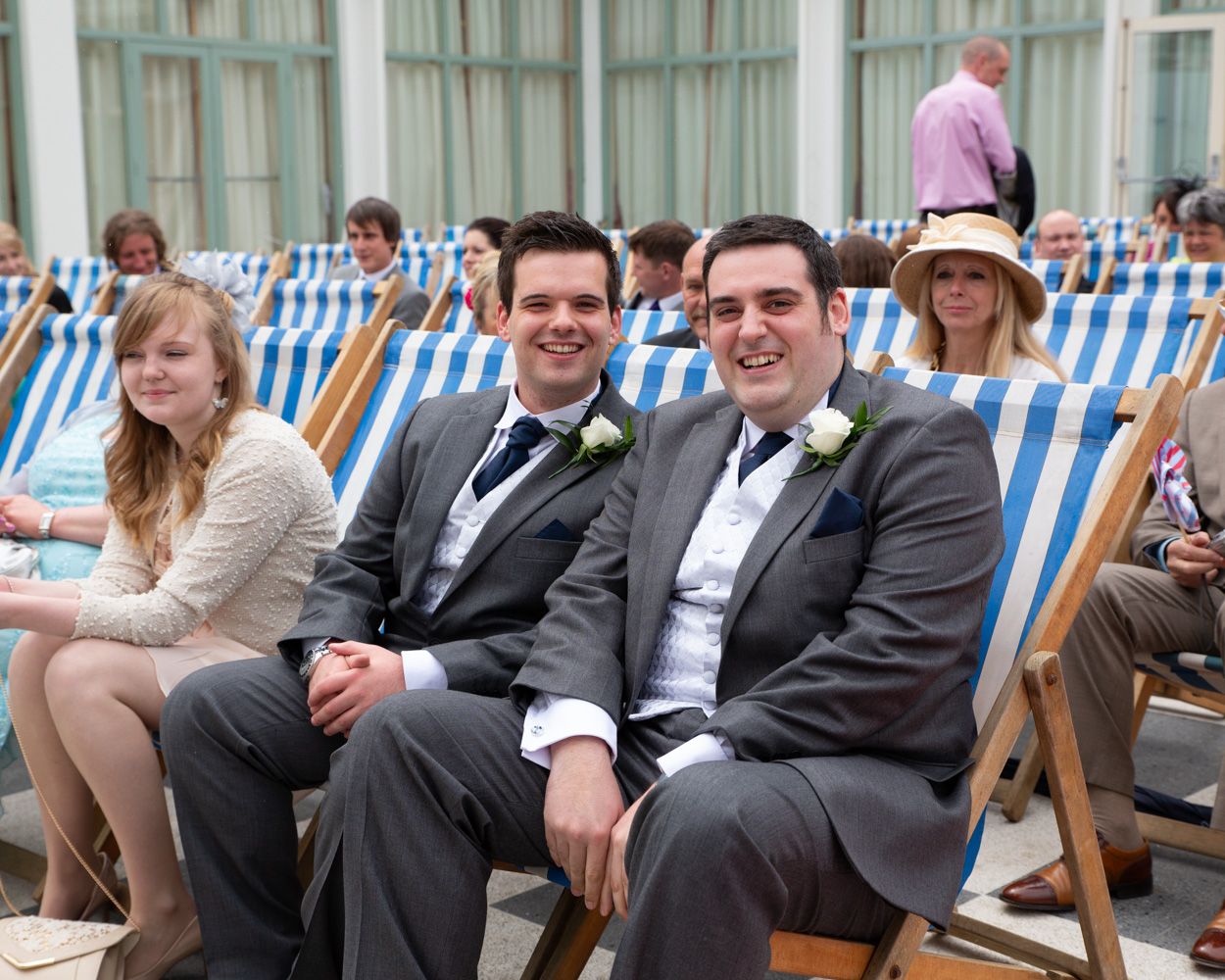 Groom and best man sitting casually among guests on deck chairs before the ceremony at Scarborough Spa.