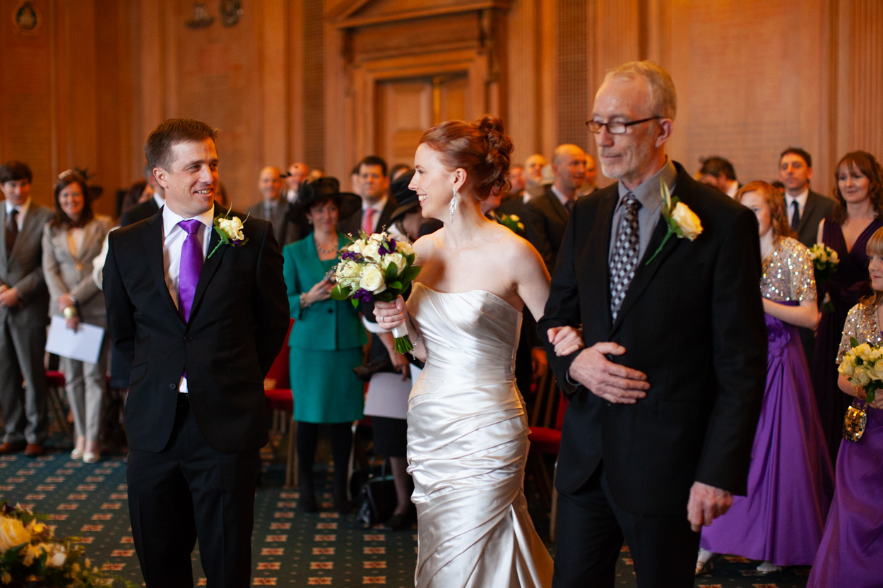 Groom turning to see his bride holding a bouquet of cream roses.