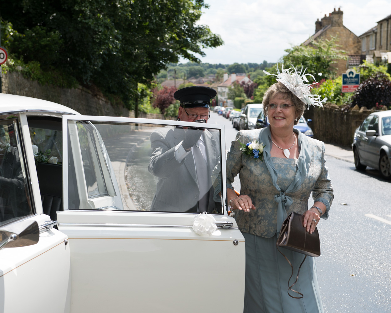 Mother of the bride steps from the car smiling toward Tanya