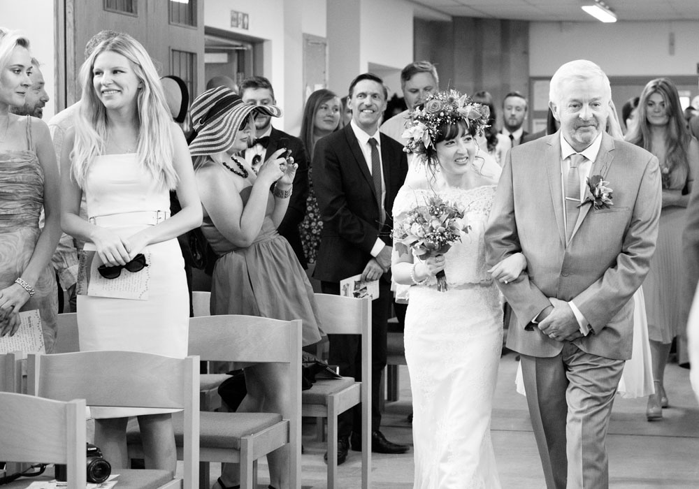 Bride and her father walk down the aisle followed by bridesmaids in black and white.