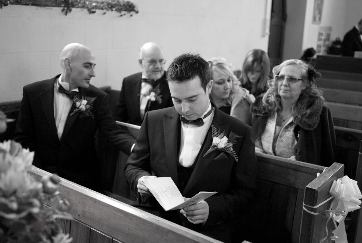 Groom sits in the pew looking over the order of service.