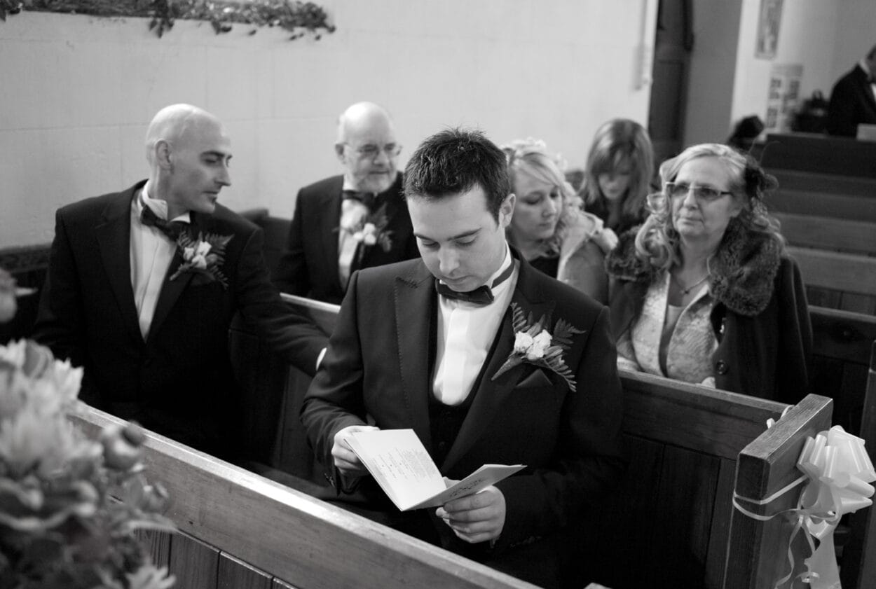 Groom sits in the pew looking over the order of service.