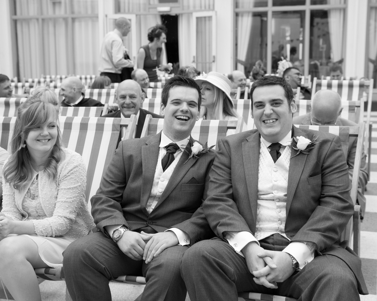 Black and white candid photo of the groom and best man smiling broadly during a relaxed moment before the ceremony.