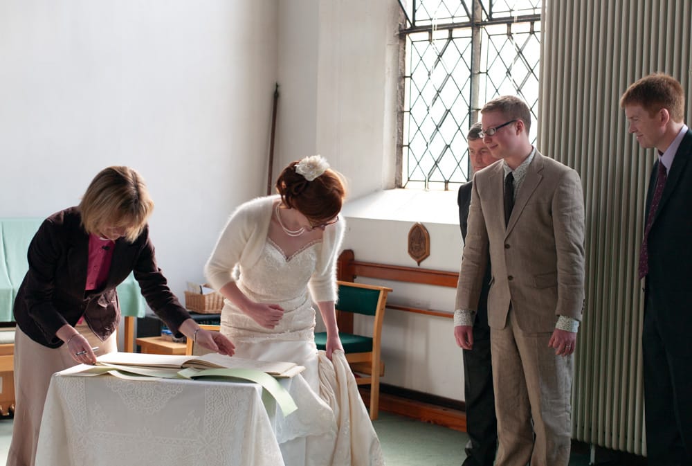 Bride with red hair sitting to sign the wedding register at St George’s.