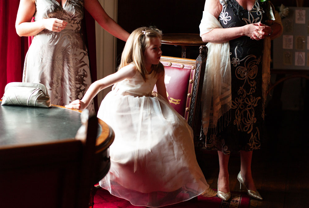 Little bridesmaid sits in her dress with satin shoes, taking a quiet moment.