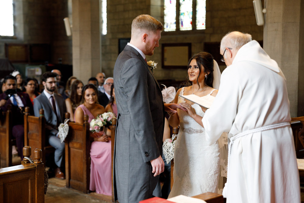 Bride places the groom’s ring on his finger, speaking directly to him with unwavering focus.