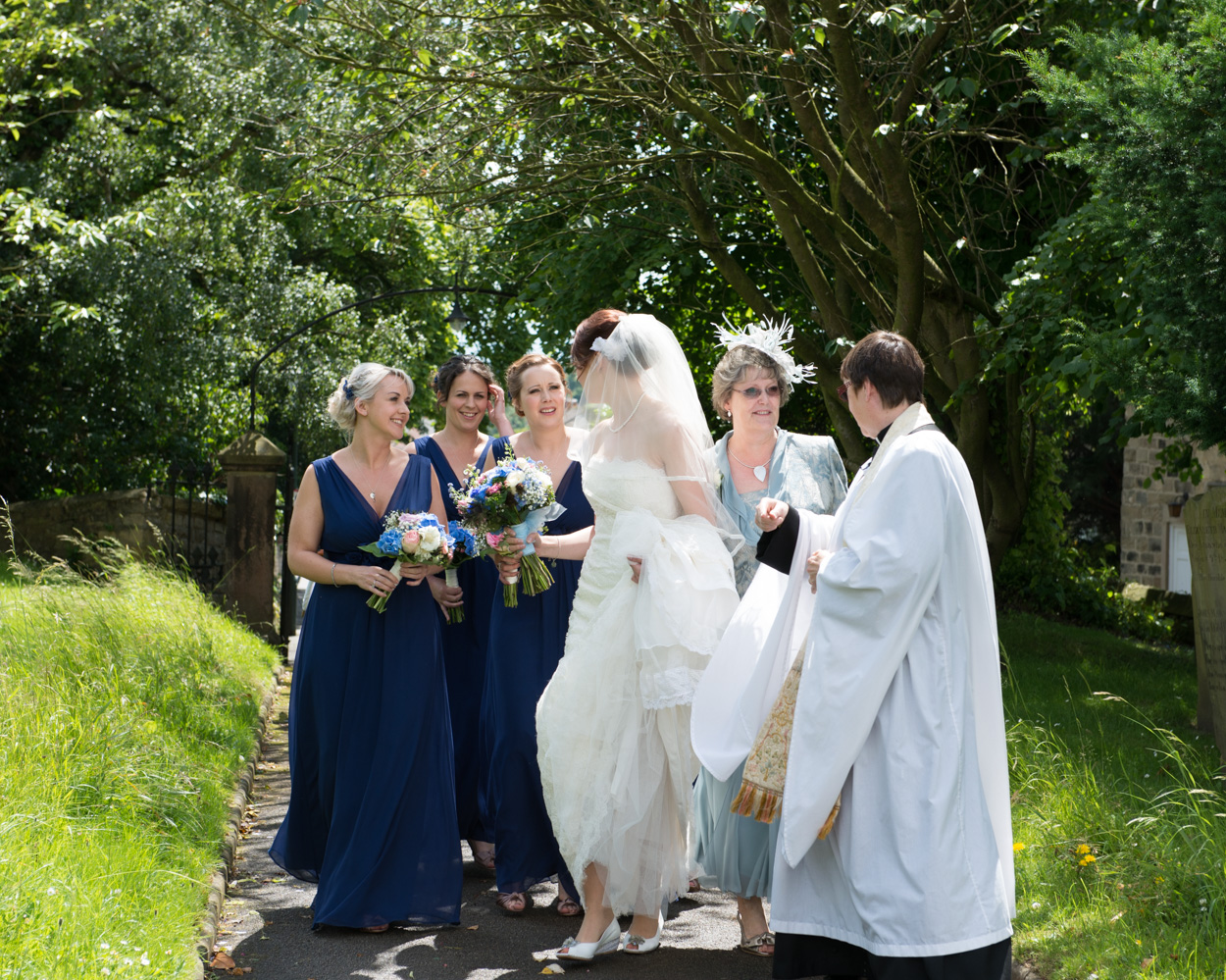 Bride and bridesmaids walk up the church path, Tanya glancing back