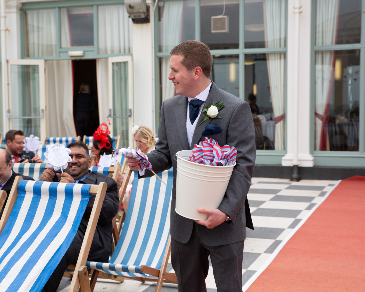 Groomsman handing out colourful sandcastle windmills to guests at a Scarborough seaside wedding.