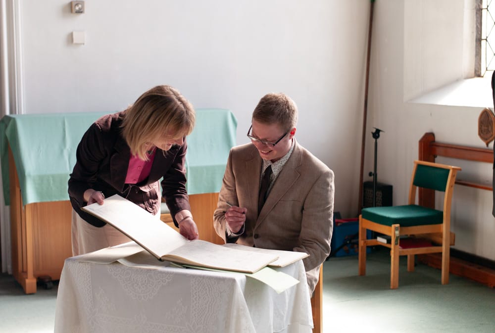 Groom smiling as he signs the wedding register in church.