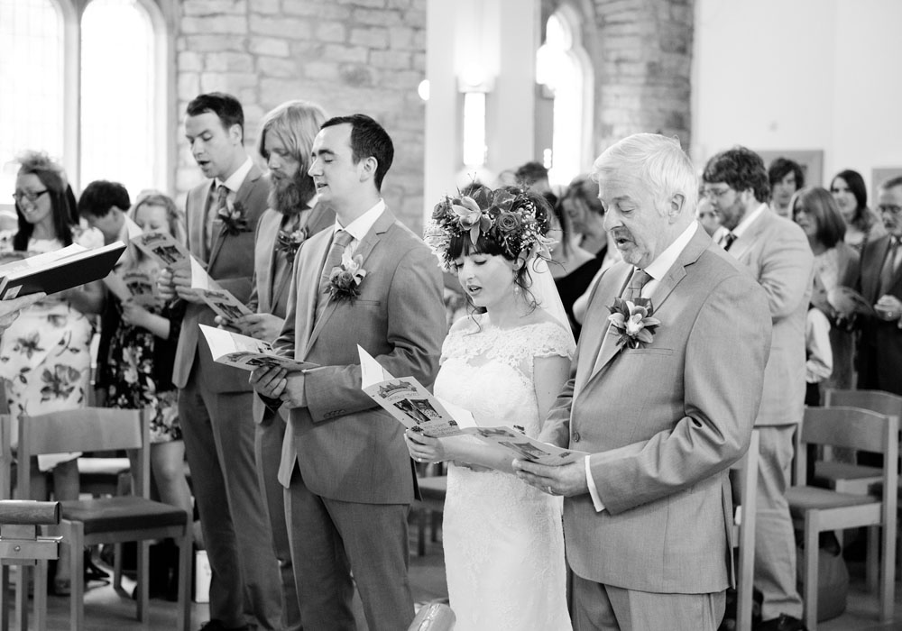 Wedding guests sing together during the church ceremony in black and white.