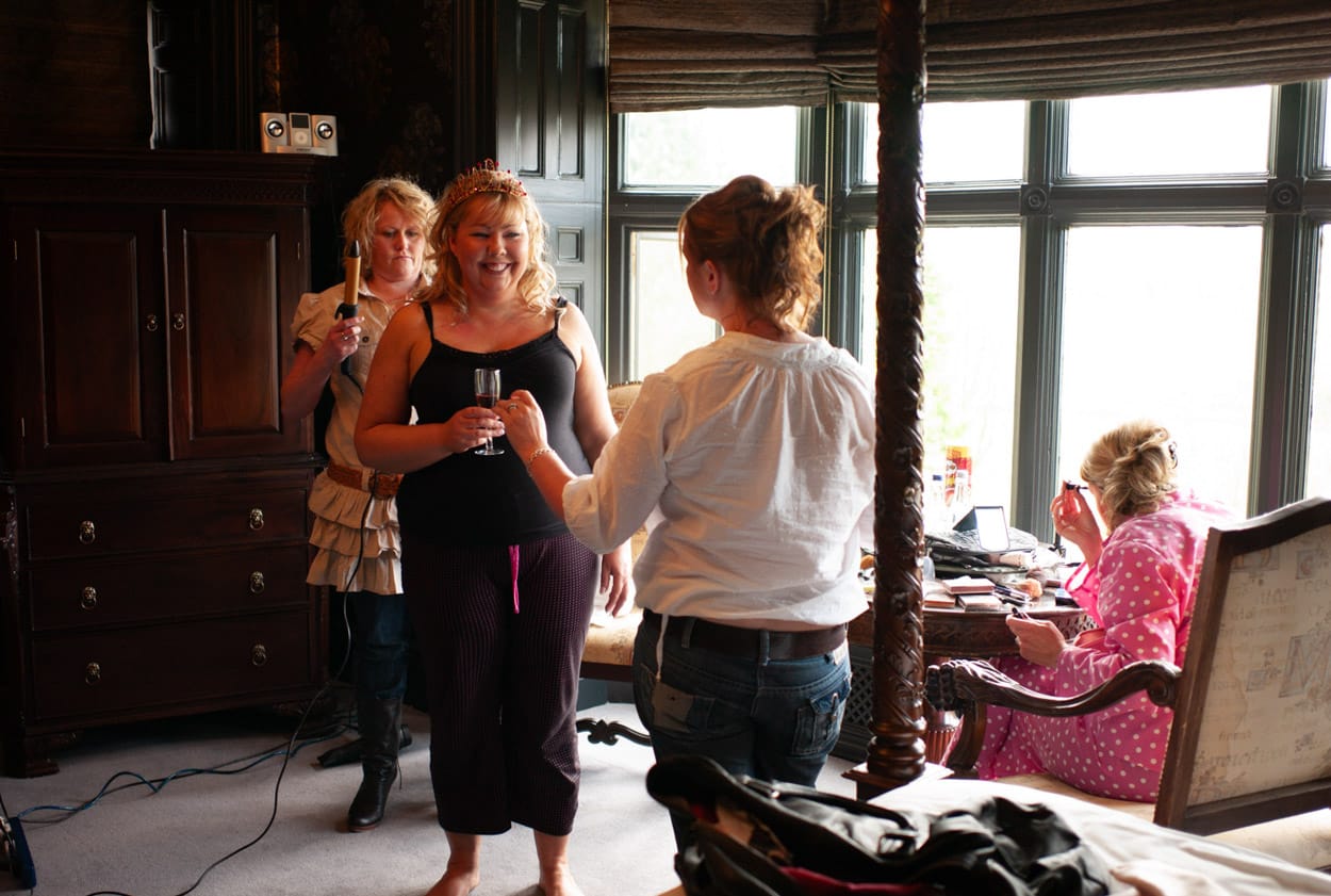 Nikki smiling in the bridal suite, dressed in black with hair in progress alongside her bridesmaids.