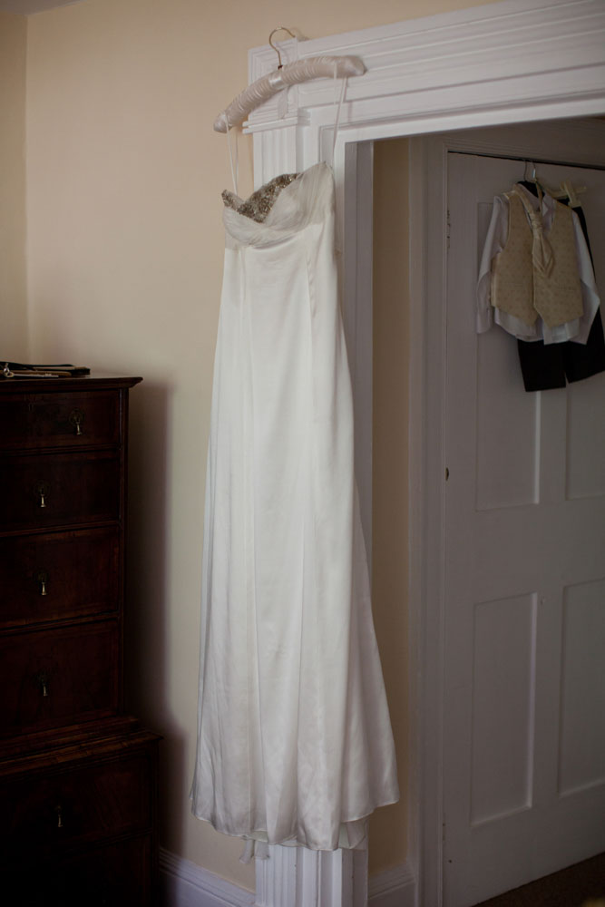 Bridal dress hung up on the door - pageboy's suit behind - natural light West Yorkshire wedding photography