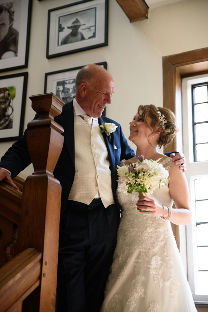 Bride’s father joins her for a photo on the stairs, smiling at each other.