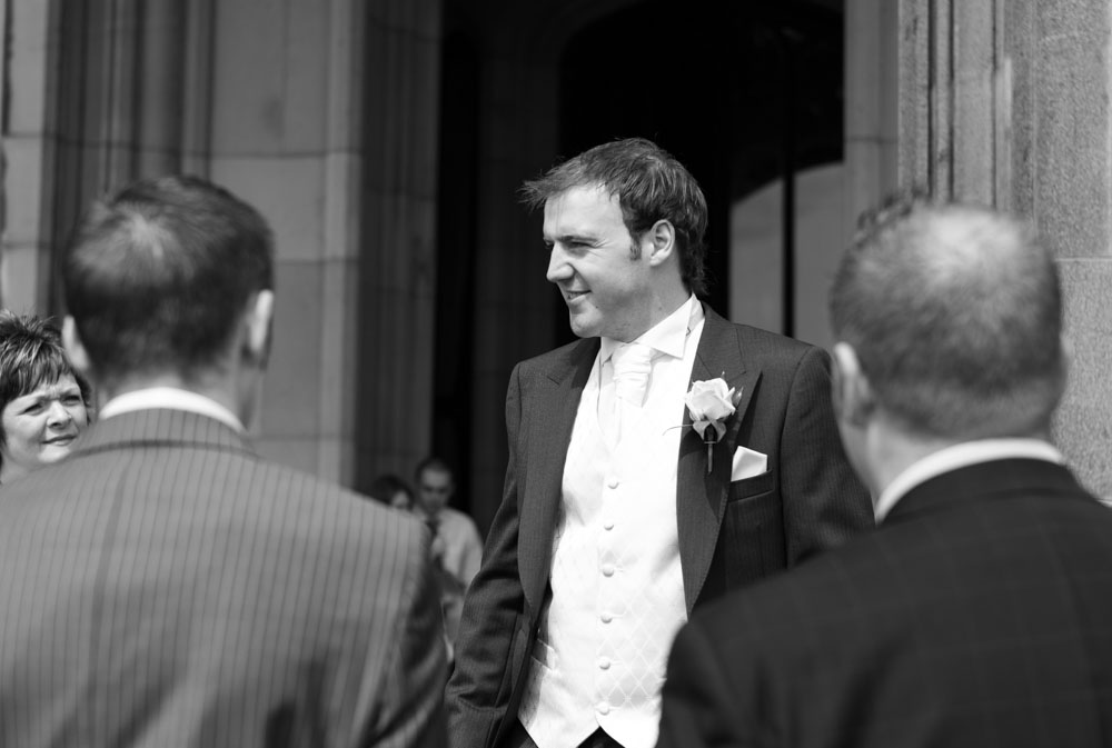 Groom framed by guests in the courtyard, captured in timeless black and white at Allerton Castle.