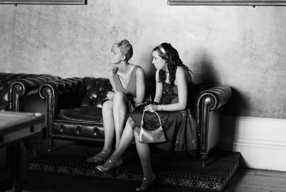 Two teenage guests sitting gracefully on a chesterfield sofa, elegant in their dresses.
