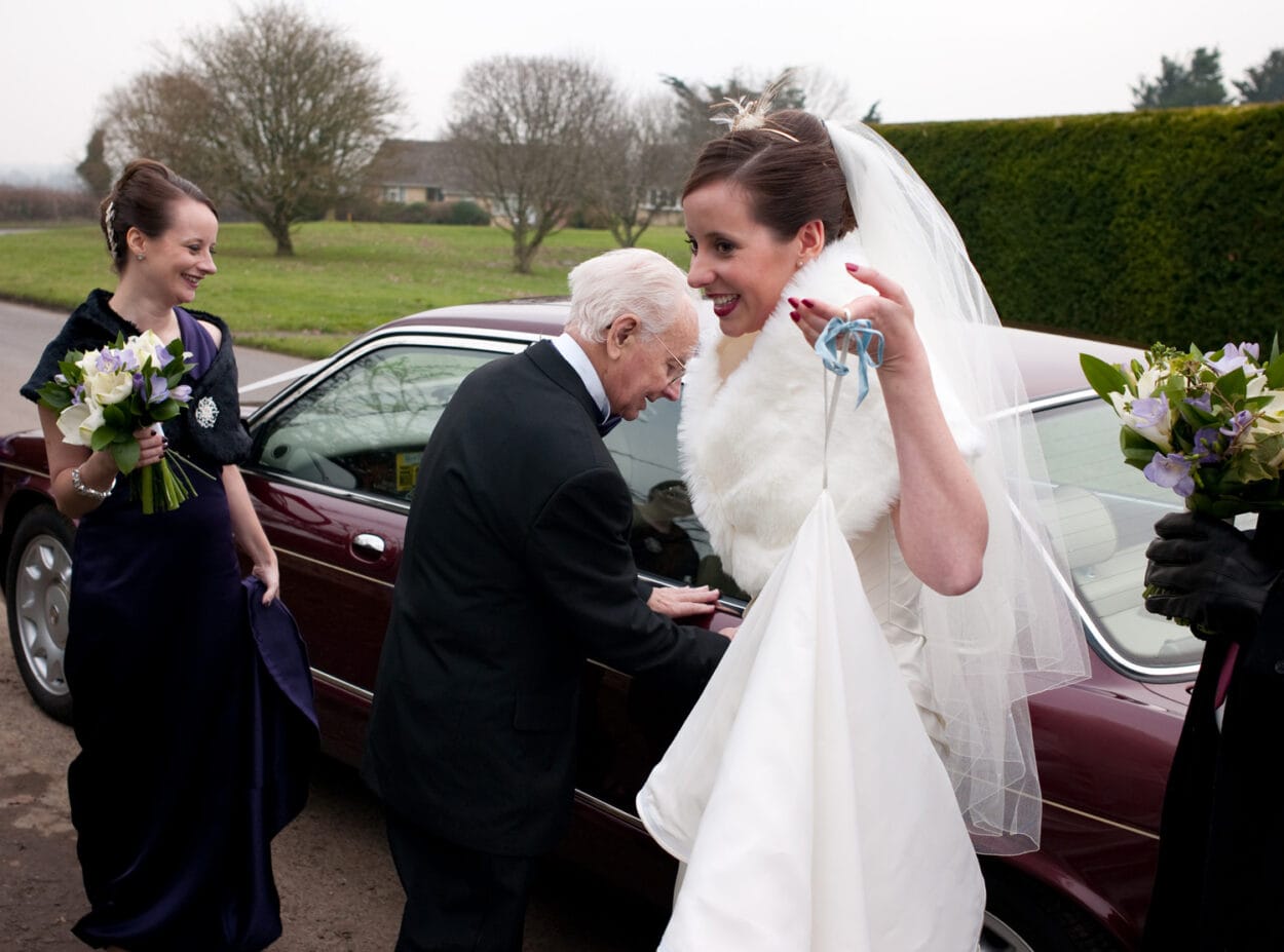 Emelie smiles holding her dress bustle as grandad closes the car door.