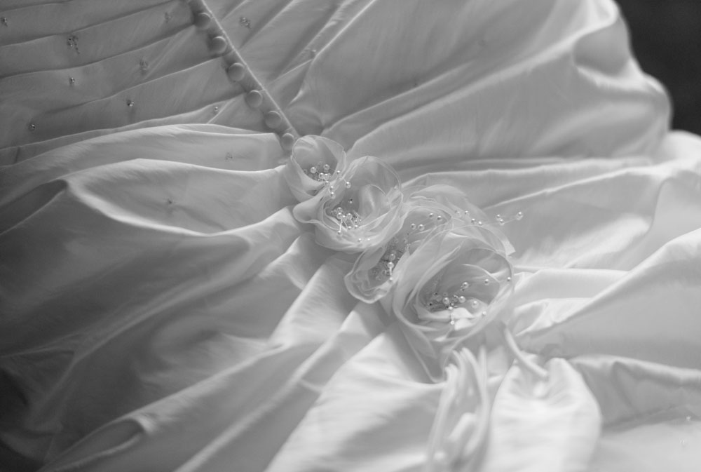 Close-up black and white of silk flower details on the bride’s dress buttons.