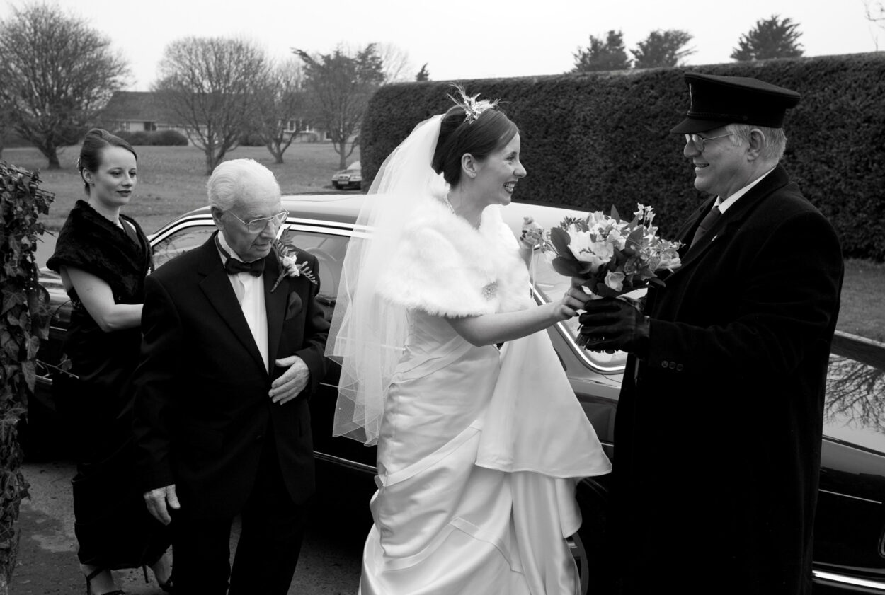 Emelie takes her bouquet from the smiling driver in monochrome.