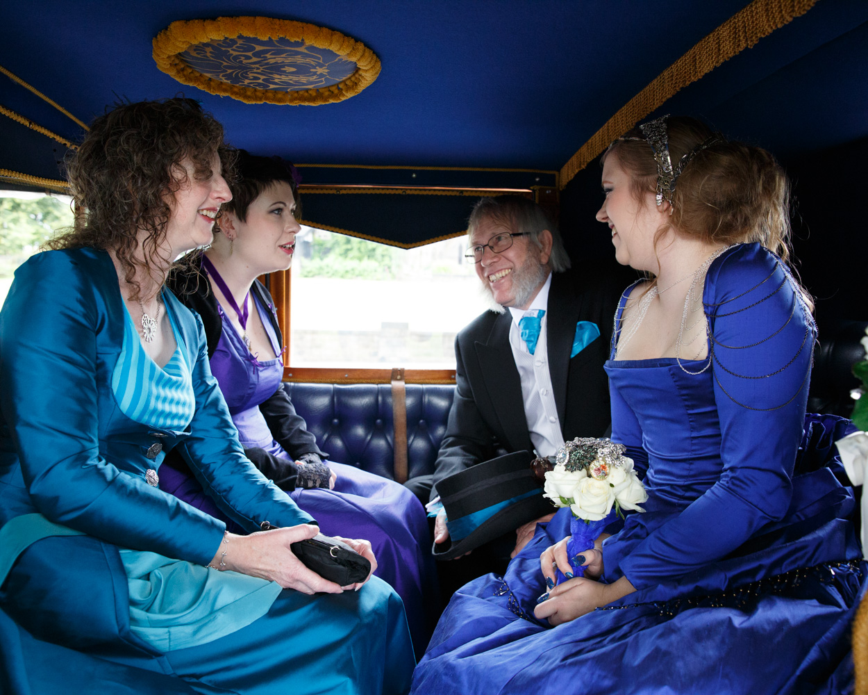The bride, bridesmaid, and father arrive in a vintage car, dressed in purple-blue tones and smiling