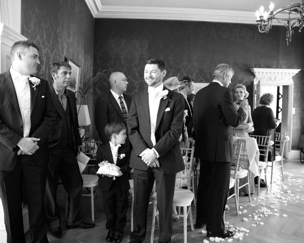 Black and white photo — groom and others turn to watch the ceremony begin.