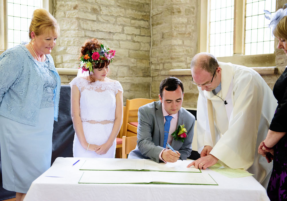 Groom signs the register as bride and mother watch on at St Paul’s Church, Huddersfield.