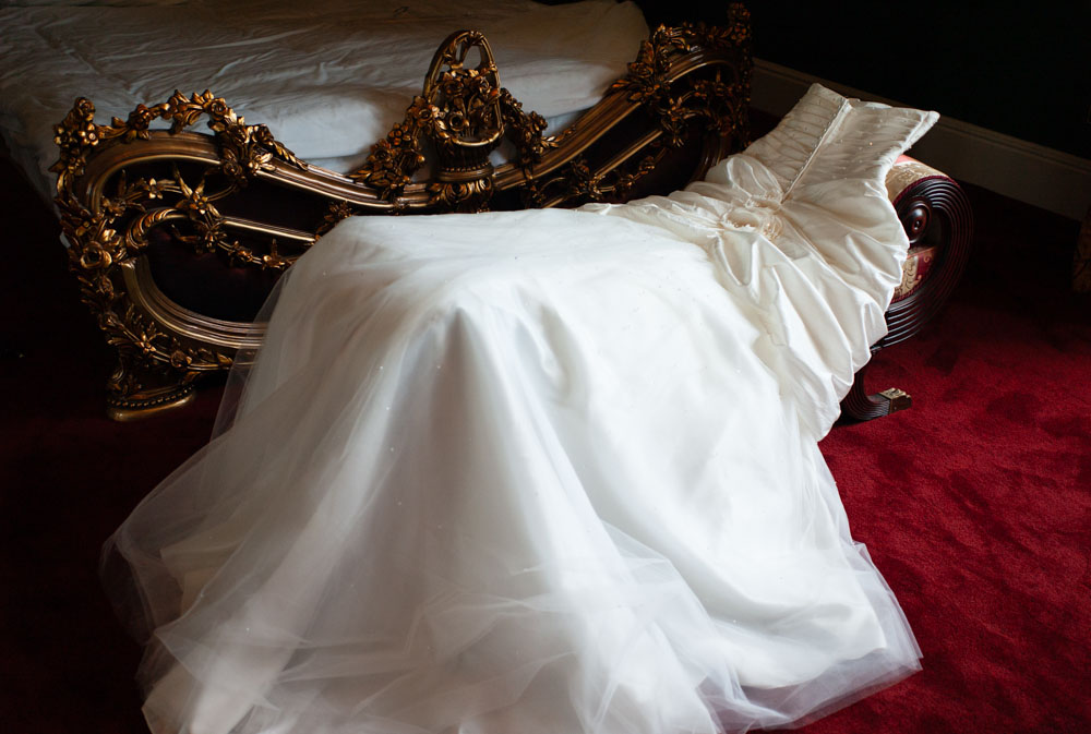Bride’s white dress displayed on a chaise lounge with gold details and red carpet beneath.