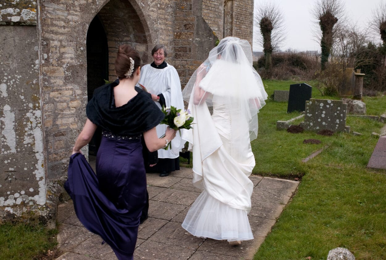 The bride, grandad, and sister meet the vicar at the entrance of the church.