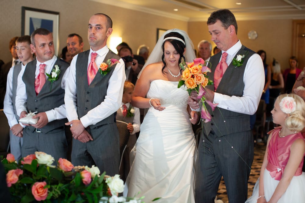 Bride hands bouquet to her father as Dave, his best man, and Gemma all share emotional smiles.