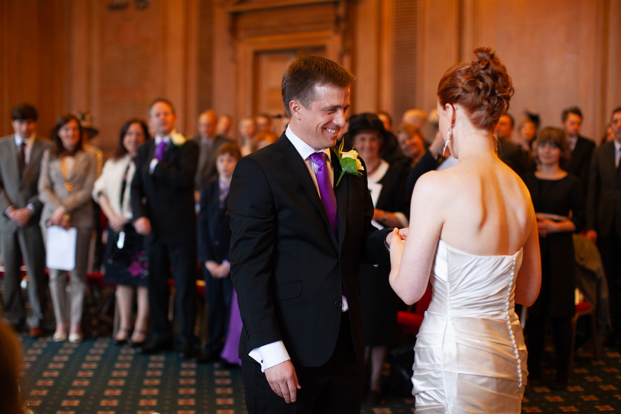 Bride placing the ring on the groom’s finger as he smiles.