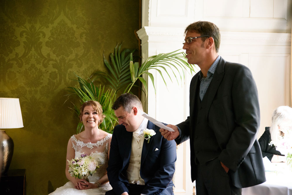 Wedding guest reads during the ceremony, making the couple smile.