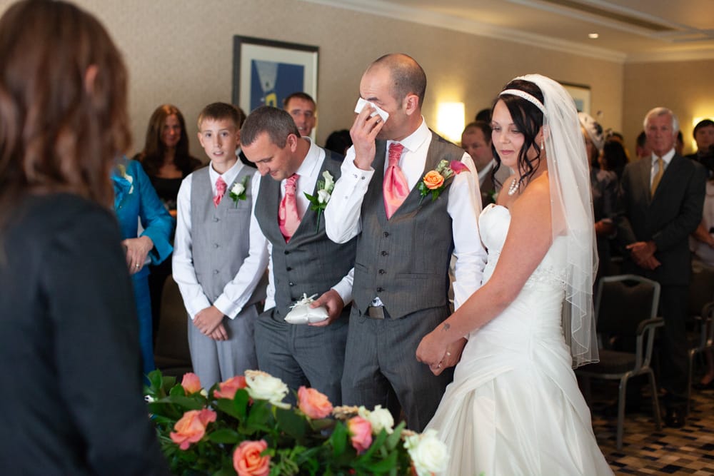 Dave wipes his eyes with a tissue while Gemma looks on with pride, surrounded by standing guests.