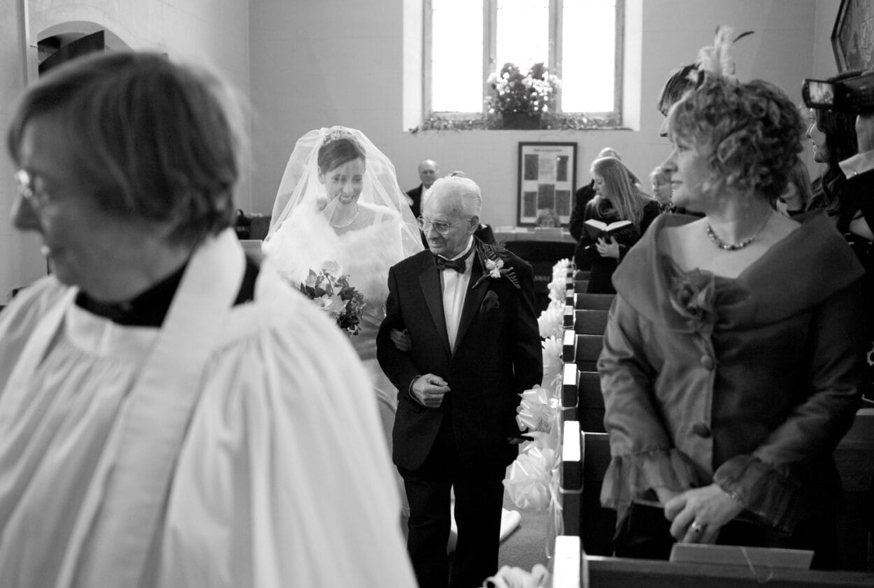 Emelie walks down the aisle smiling as guests look on.