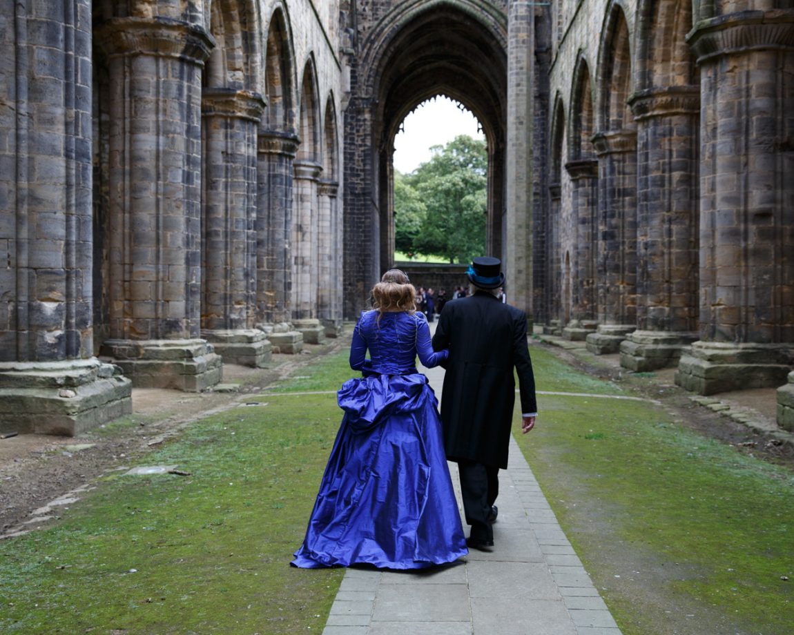 028 from behind they continue walking framed by the abbey columns and arches kirkstall abbey wedding linsey and chris