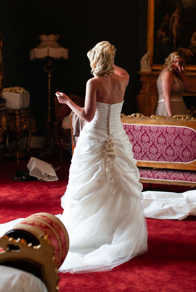 Color image of bride’s back in her dress surrounded by rich red and gold room decor.