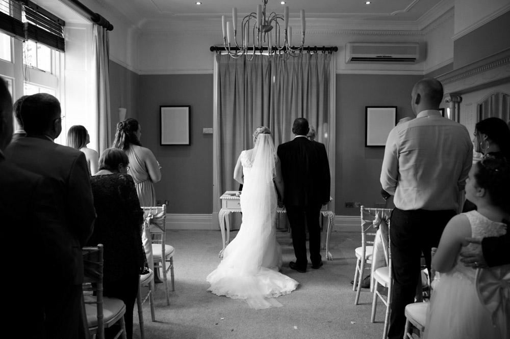 Black and white view from behind as Tracy walks down the aisle, veil trailing