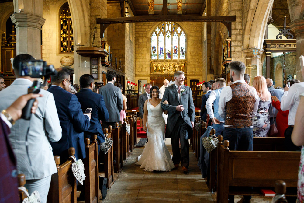 The newlyweds begin their walk back down the aisle, smiling at their friends and family.
