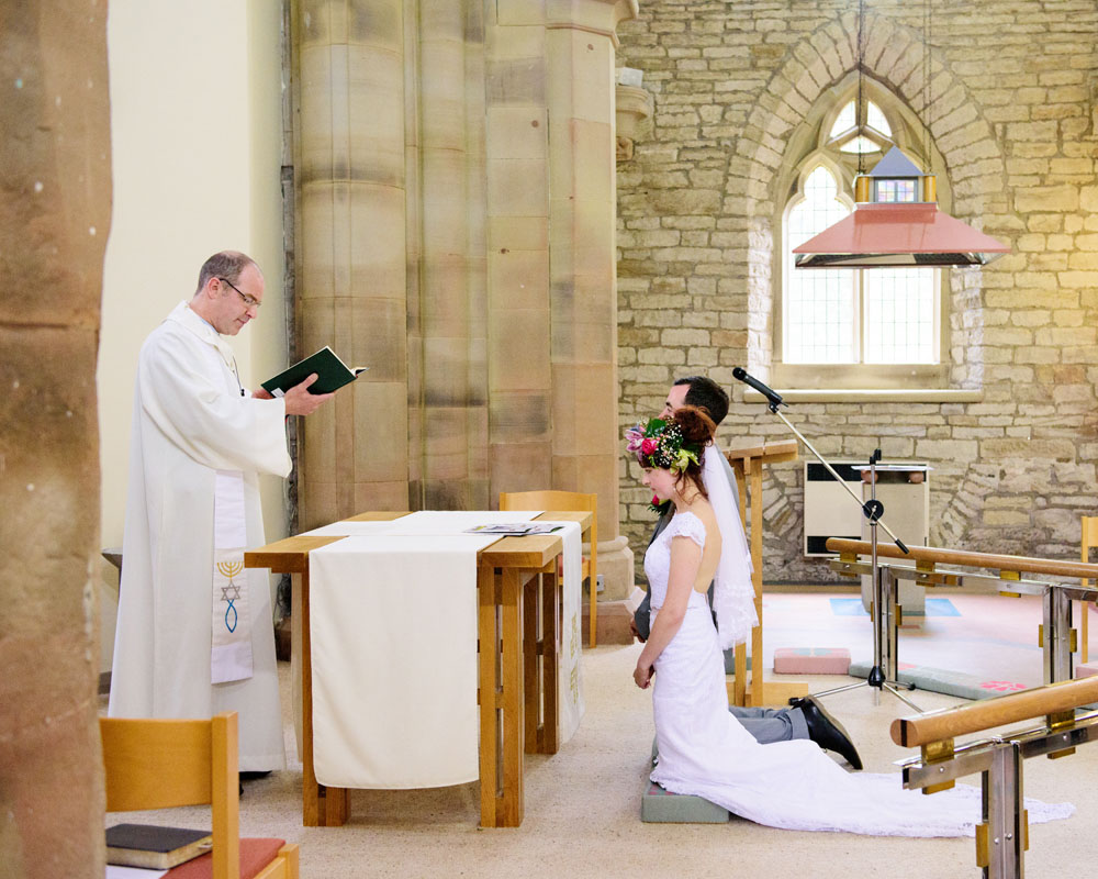 Bride and groom kneel at the altar as they receive a blessing during their West Yorkshire church wedding.