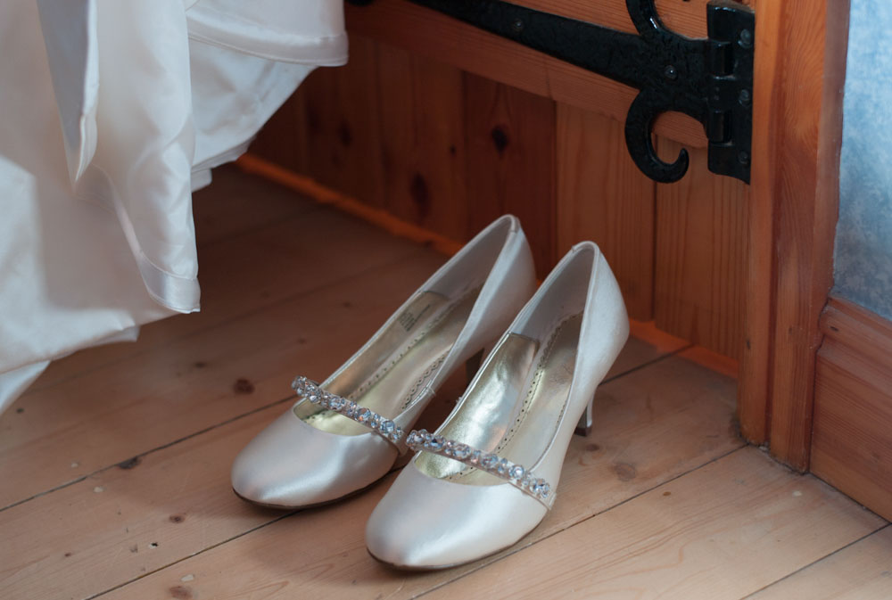 Bridal shoes placed on wooden floorboards near the window.