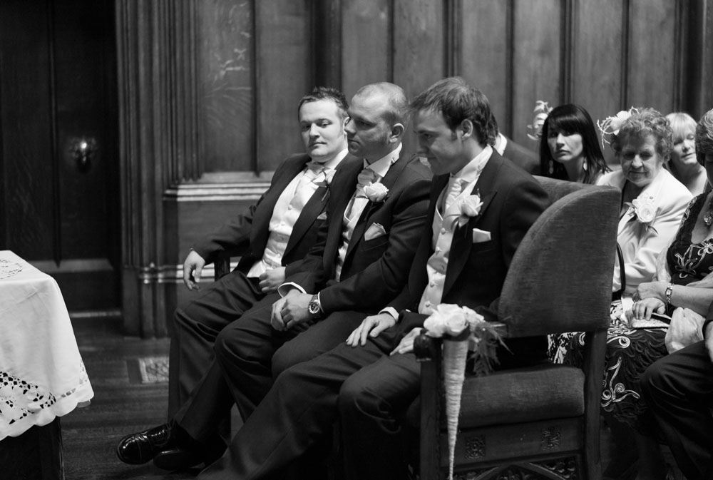 Groom and best man seated in the ceremony room, black and white, the groom showing a brief moment of stress.