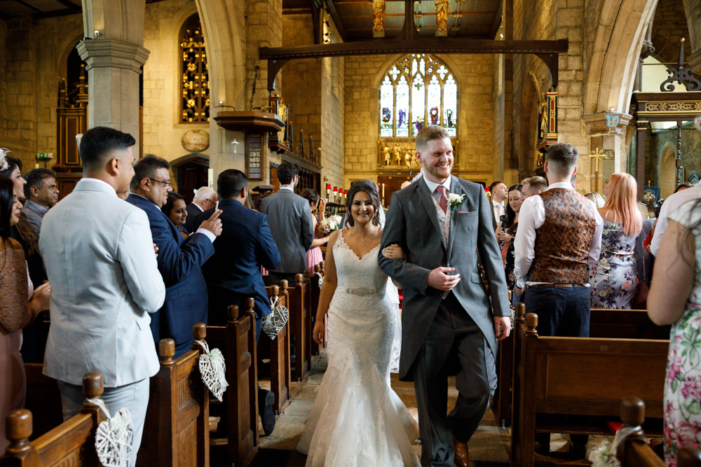 Kyra and Matt smile as they approach the end of the aisle, surrounded by joy.

